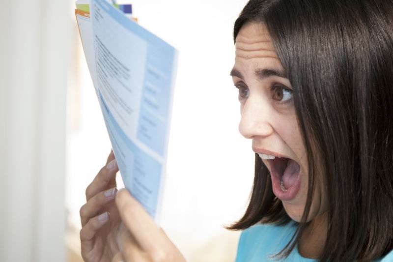 Young woman expressing shock at the price of a bill.