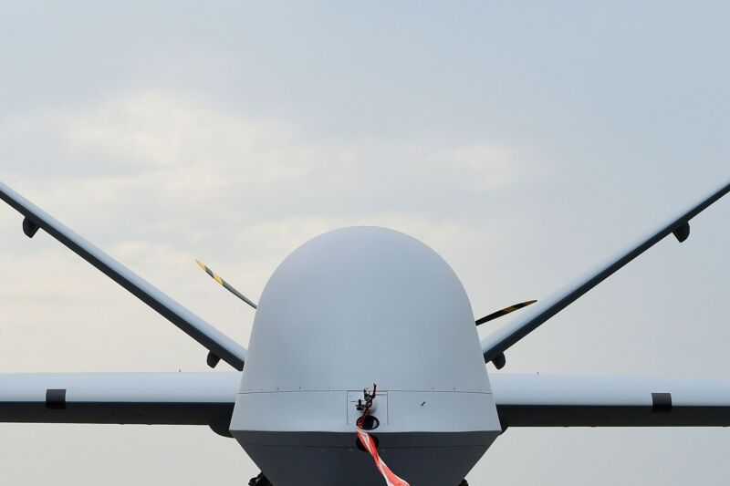 A military drone is faceless and menacing against a mostly blue sky.