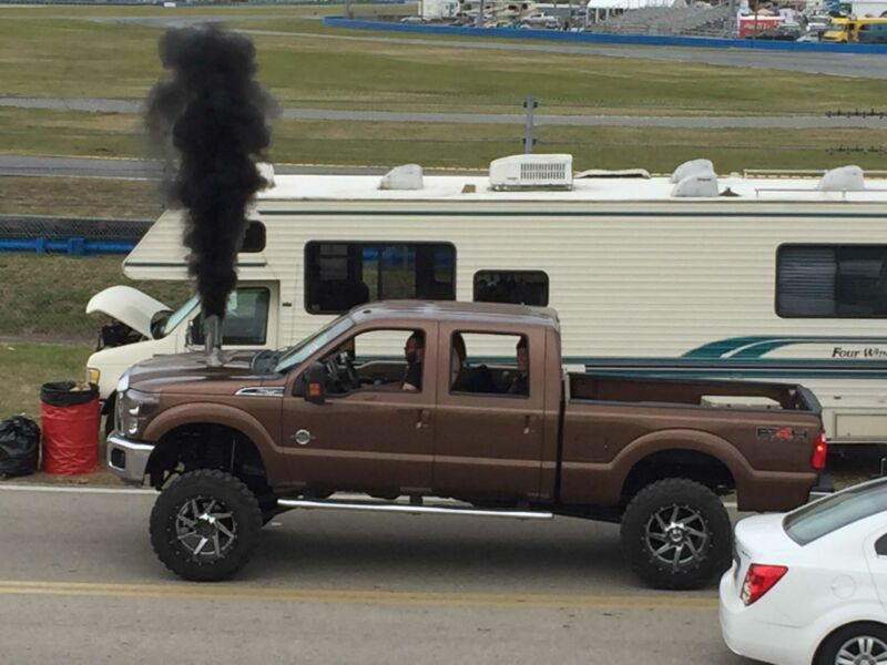 A pickup truck emits a huge black cloud of soot from an exhaust cut into its hood.