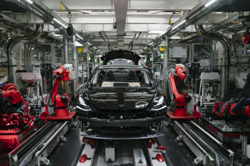 Robotic arms surround an incomplete sedan.