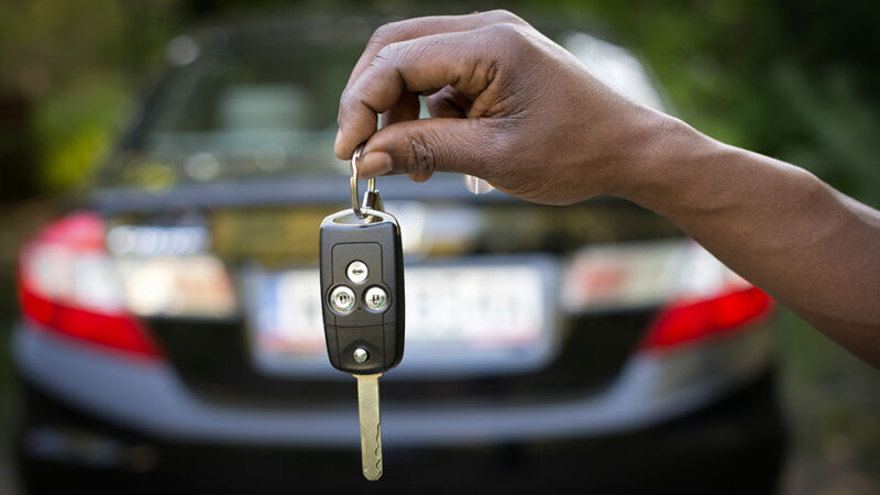 Stock photo of a dark-skinned hand holding out a set of car keys.